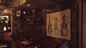 A dimly lit bar area with wooden furniture, stone walls, and a large poster of a mechanical device.