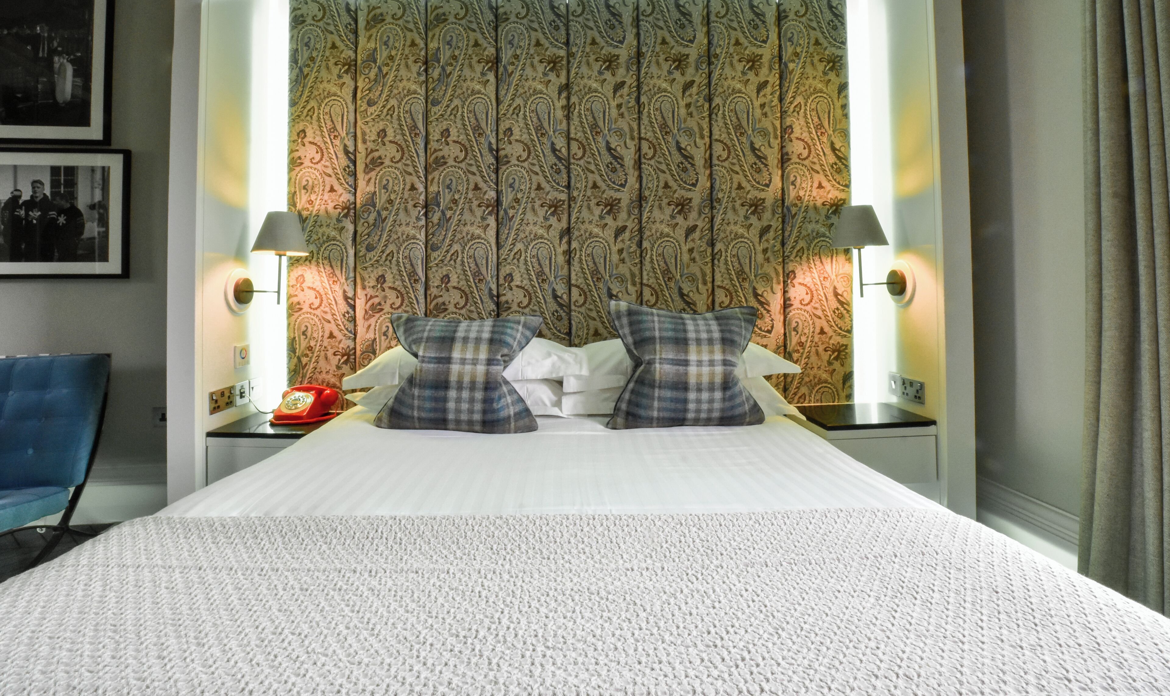 A hotel room with a large bed, two bedside lamps, a red telephone, and a patterned wallpaper.