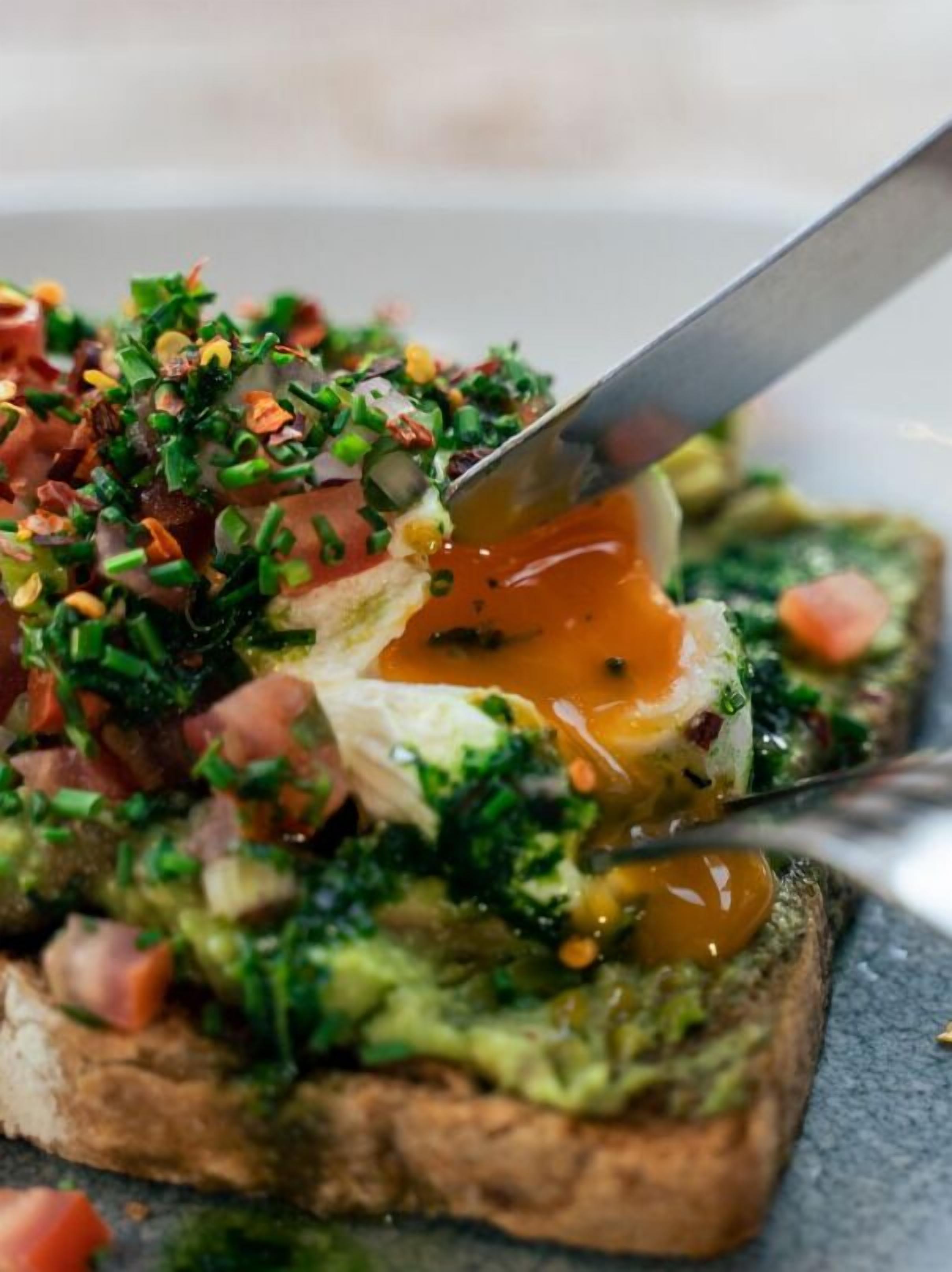 A close-up of a dish with a poached egg on toast, garnished with chopped herbs and diced tomatoes.
