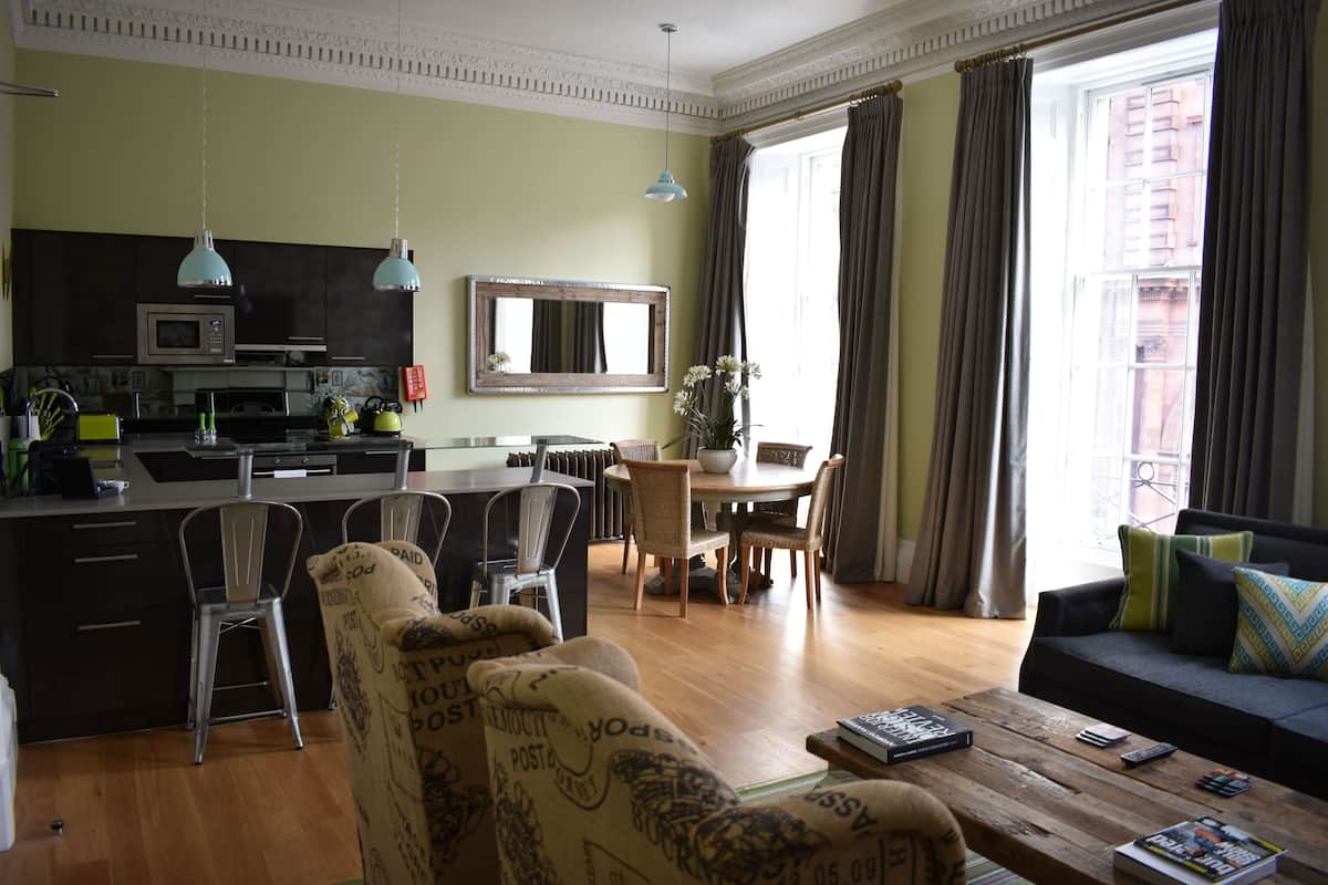 A modern living room with a dining area, kitchen, and large windows.