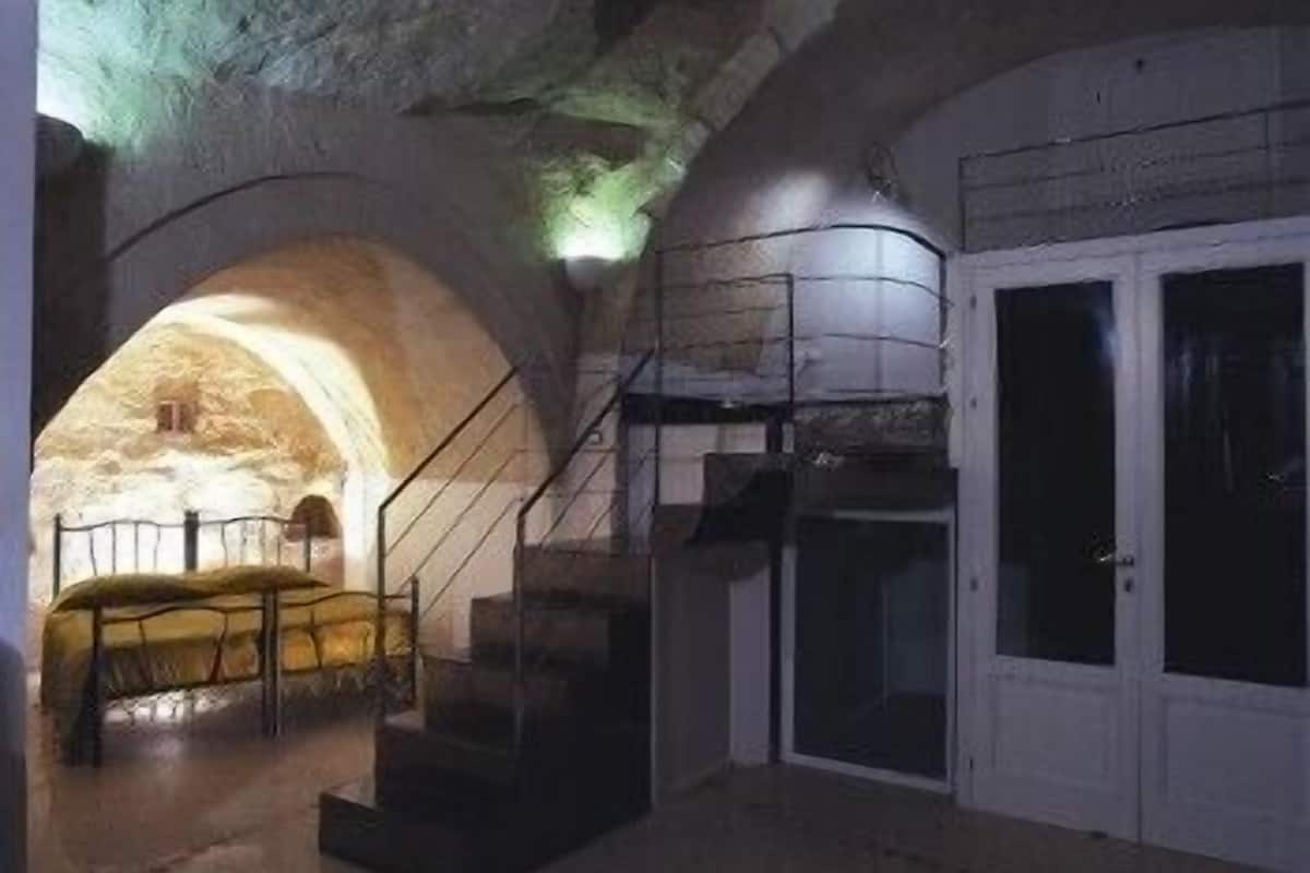 Un interior con una escalera que lleva a una plataforma, una puerta y una pared de piedra con una abertura arqueada.