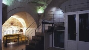 An interior with a staircase leading to a landing, a door, and a stone wall with an arched opening.