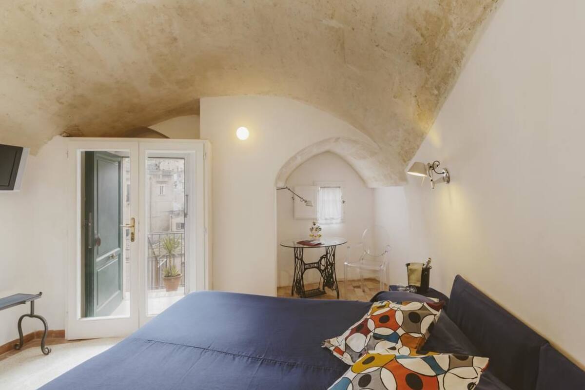Un dormitorio con una cama grande, una puerta que da a un balcón, una mesita con una silla y una máquina de coser.