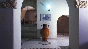 An arched doorway leading to a room with a tiled floor and a large vase in the center.