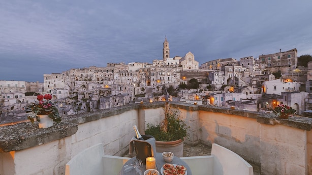 A rooftop terrace with a table set for a meal, a bottle of champagne, and a view of a historic cityscape.