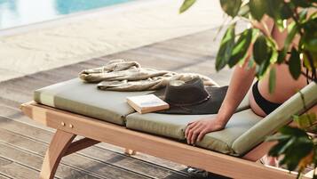 A wooden lounge chair with a cushion, a book, and a hat placed on it.