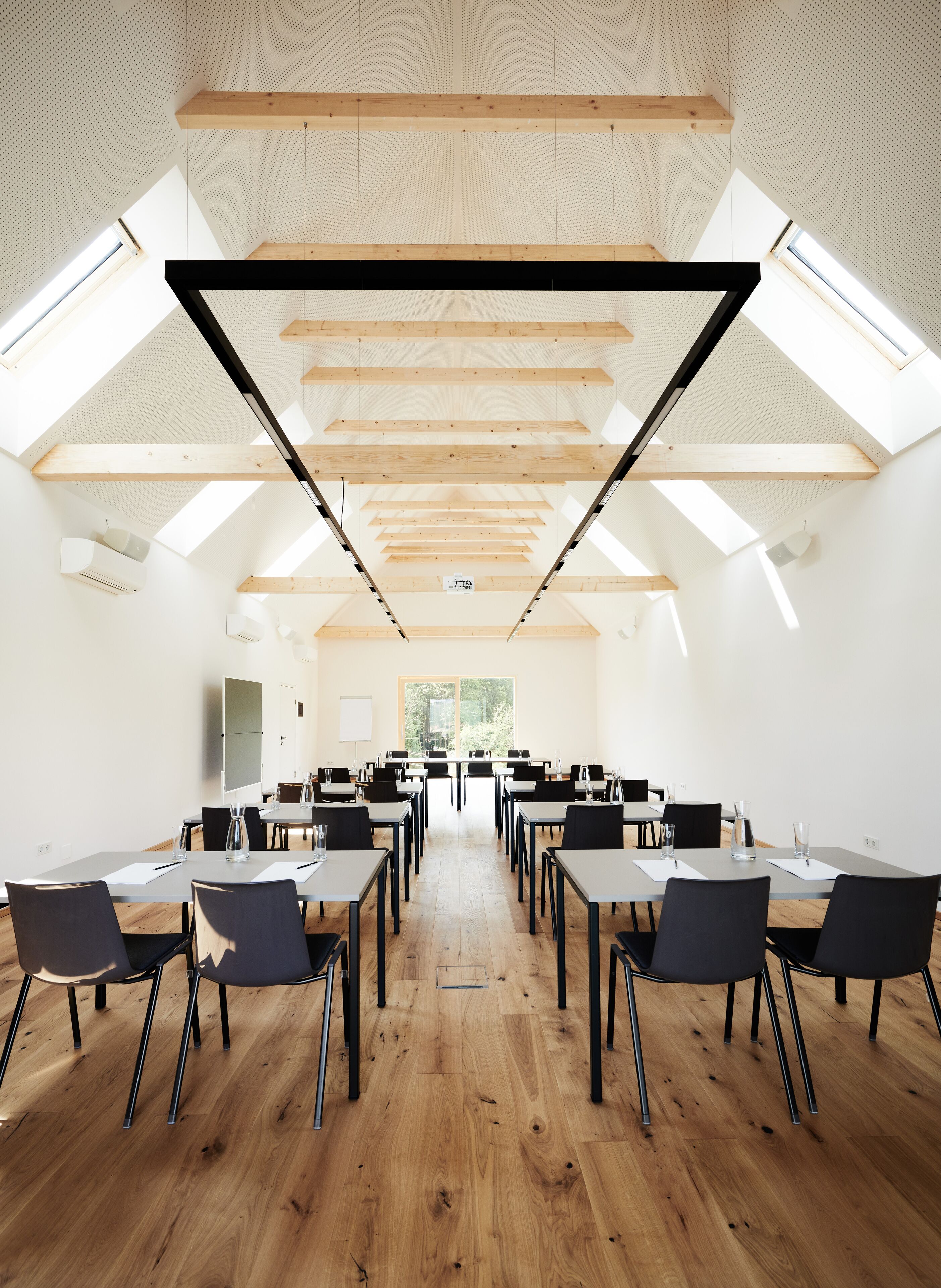 A conference room with a high ceiling, wooden beams, and skylights. Tables and chairs are arranged for meetings.