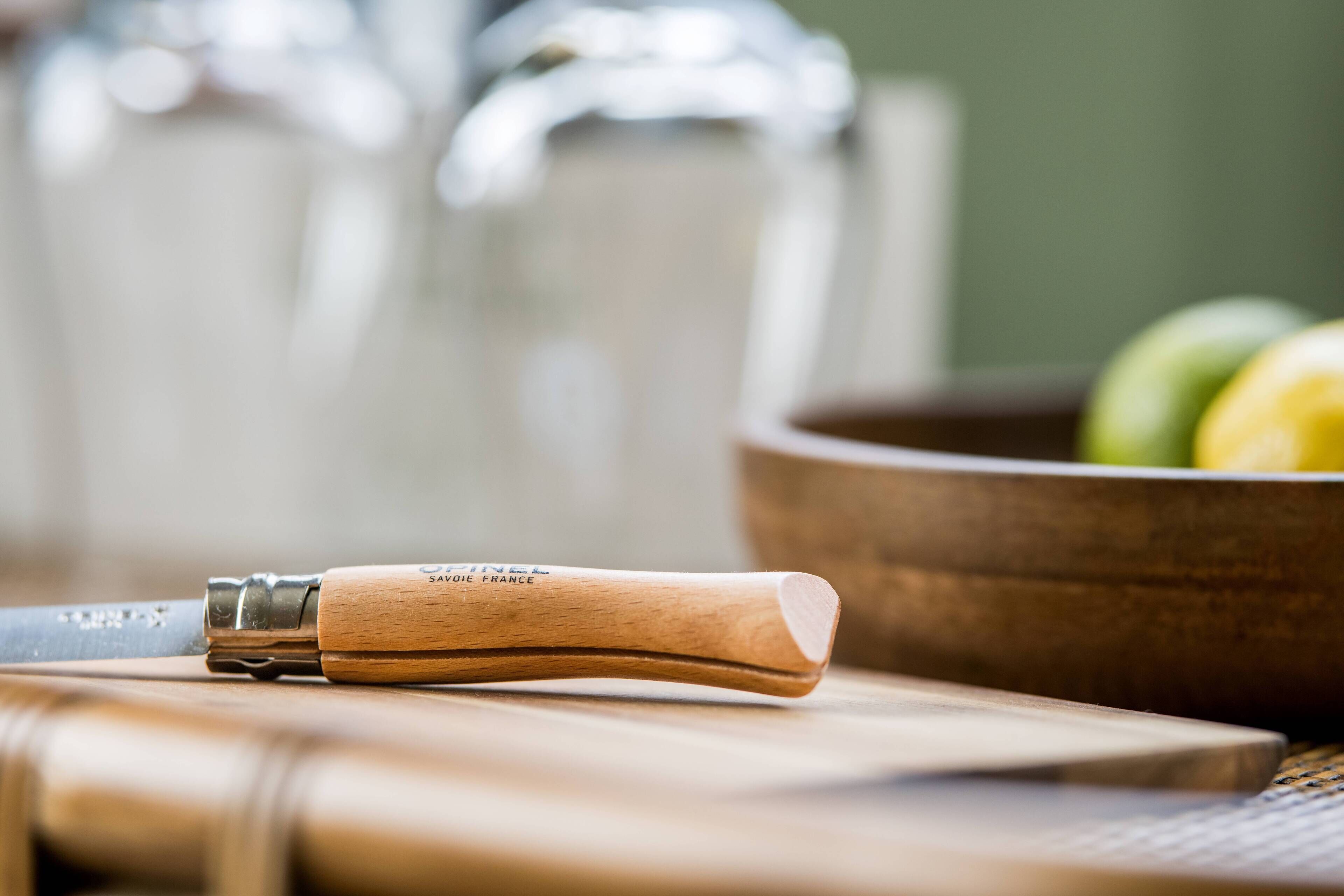 Uma faca de cabo de madeira sobre uma tábua de corte, com um fundo desfocado de uma tigela e recipientes de vidro.