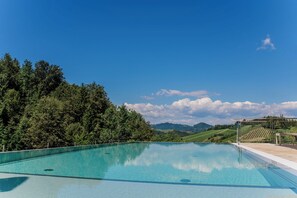 A clear blue swimming pool with a wooden deck and a pergola, surrounded by lush greenery and hills in the background. - Landgut am Pößnitzberg (Leutschach)