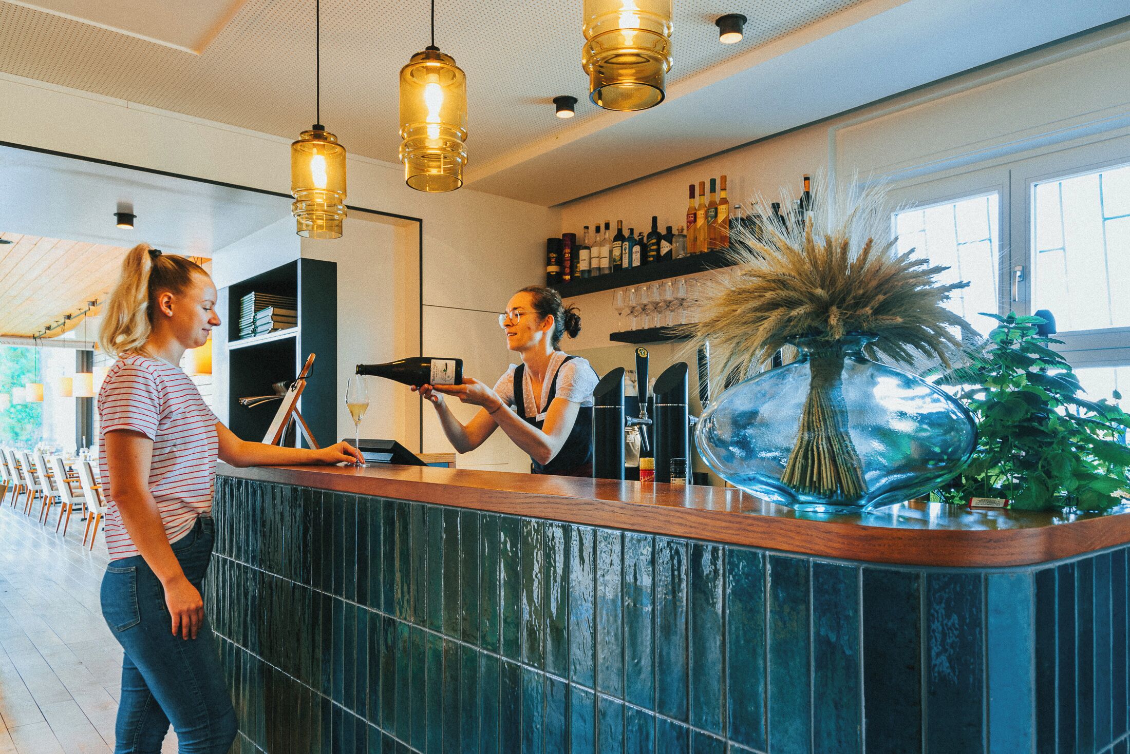 A bar area with a counter, hanging light fixtures, and a shelf with bottles.