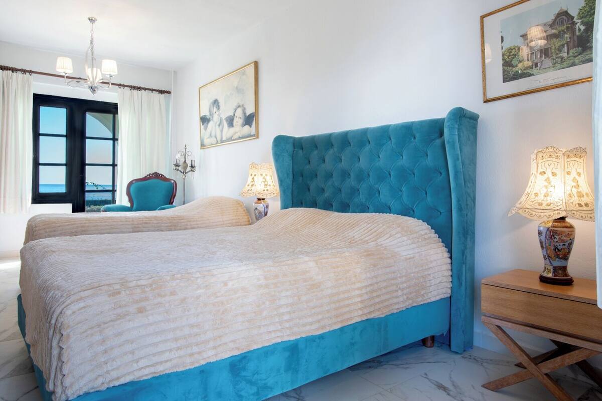 A bedroom with two beds, a chandelier, a framed picture, and a lamp.
