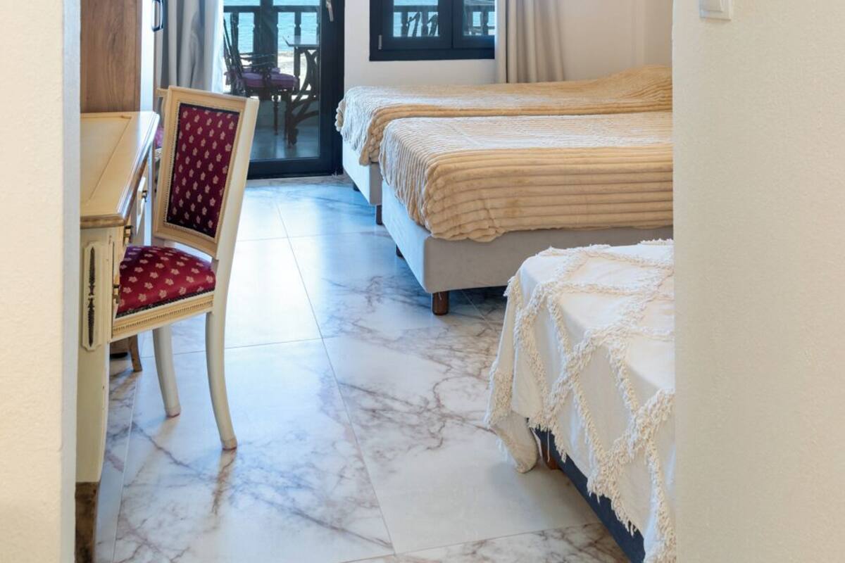 A bedroom with two beds, a chair, and a view of the sea through a balcony.