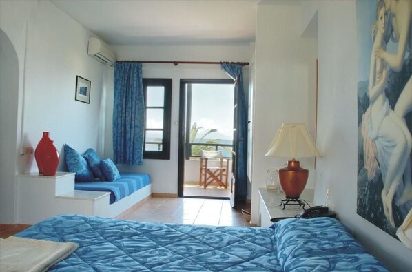 A bedroom with a bed, a desk, a chair, a painting, and a balcony with a view. - Assa Maris Beach Hotel (Sithonia)