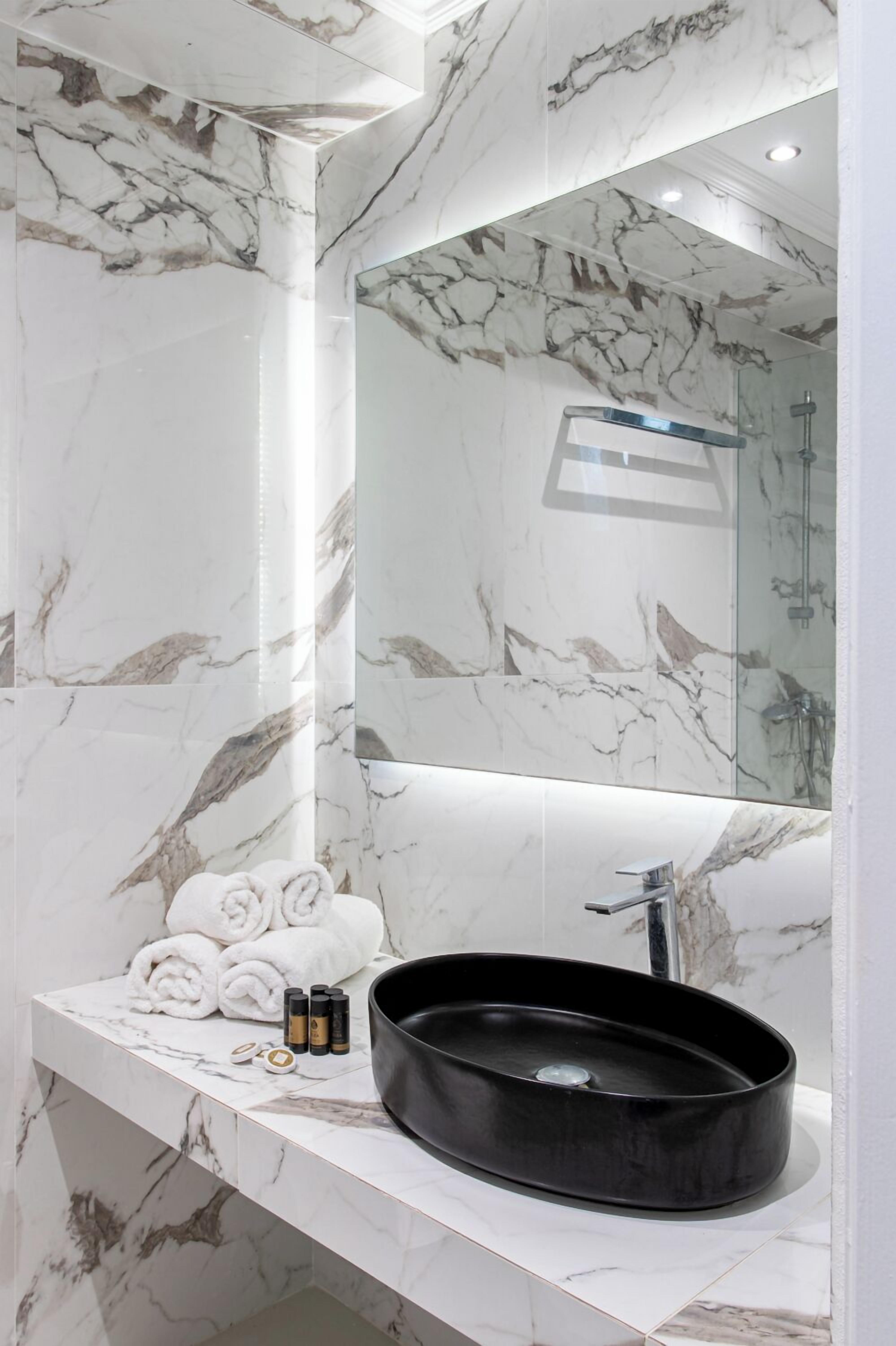 A bathroom with a marble wall, a black sink, and a mirror.