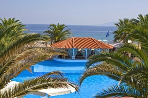 A pool with a tiled roof structure, surrounded by palm trees and overlooking the sea. - Assa Maris Beach Hotel  (Sithonia)
