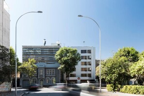 A street view with modern buildings, a clear sky, and a tree-lined sidewalk. - Hotel Nippon (Santiago)