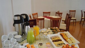 Un tavolo per buffet con diversi cibi, tra cui panini, frutta e dolci, e un angolo caffè con bollitore e thermos.