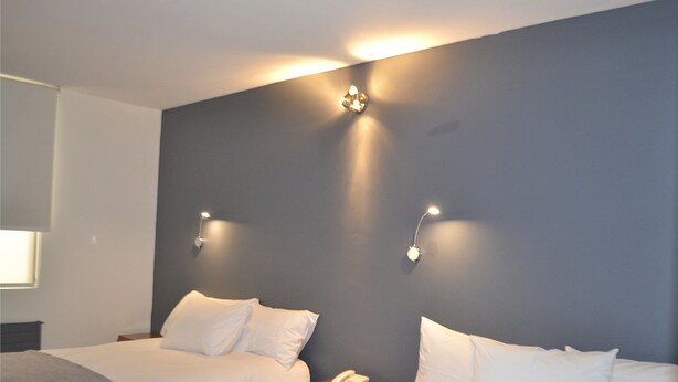Camera d'albergo con due letti, un comodino con il telefono e illuminazione a parete.