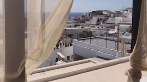 A view from a window with sheer curtains, overlooking a cityscape with buildings and a clear sky. - Xenones Lindos (Rhodes)