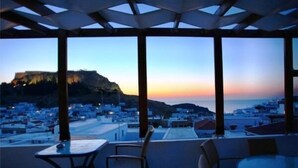A terrace with tables and chairs overlooking a coastal town at sunset. - Xenones Lindos (Rhodes)