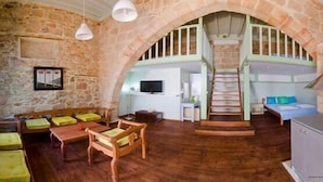 A rustic stone interior with wooden furniture, a staircase, and a television. - Xenones Lindos (Rhodes)