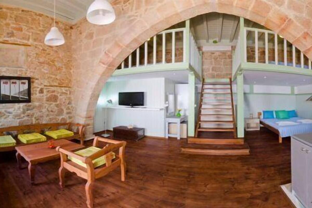 A rustic stone interior with wooden furniture, a staircase, and a television.