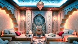 A luxurious spa room with a central fountain, two sofas with towels, and patterned walls.