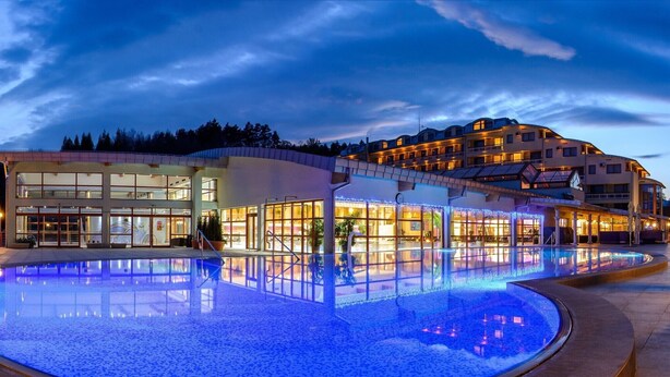 A hotel with a large pool, a modern building with glass windows, and a well-lit exterior.