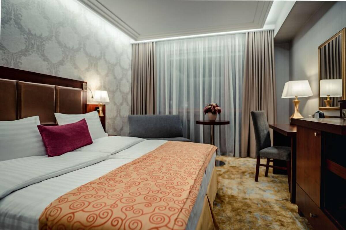 Une chambre d’hôtel avec un grand lit, un bureau, une chaise, une petite table avec une lampe et un miroir.