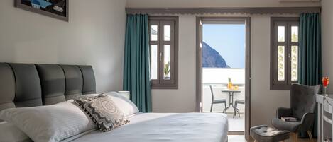 Quarto de hotel com cama, escrivaninha e varanda com vista para o mar.