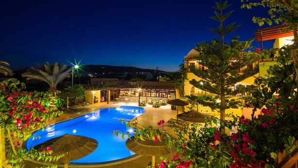 A nighttime view of a resort with a swimming pool, outdoor seating, and lush greenery. - Smaragdi Hotel (Santorini)
