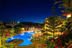 Ein Nachtbild eines Resorts mit Schwimmbad, Außenbereich und üppiger Vegetation.