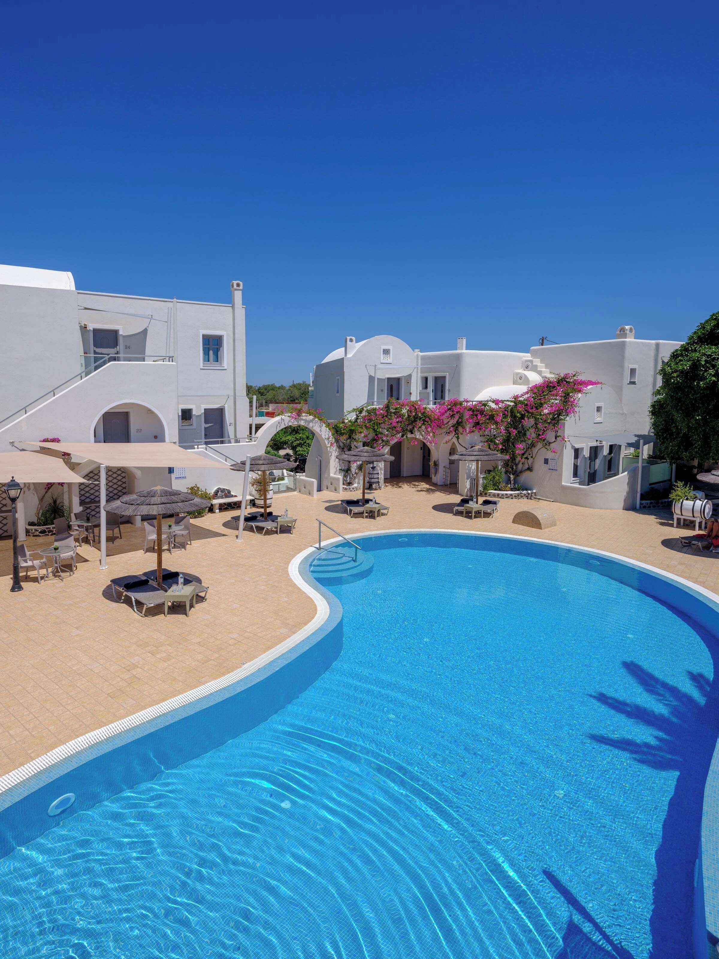 A swimming pool with a curved edge, surrounded by white buildings with arched doorways and balconies.