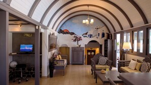 A spacious living area with a high arched ceiling, a fireplace, a television, and a dining area with a table and chairs. - Smaragdi Hotel (Santorini)