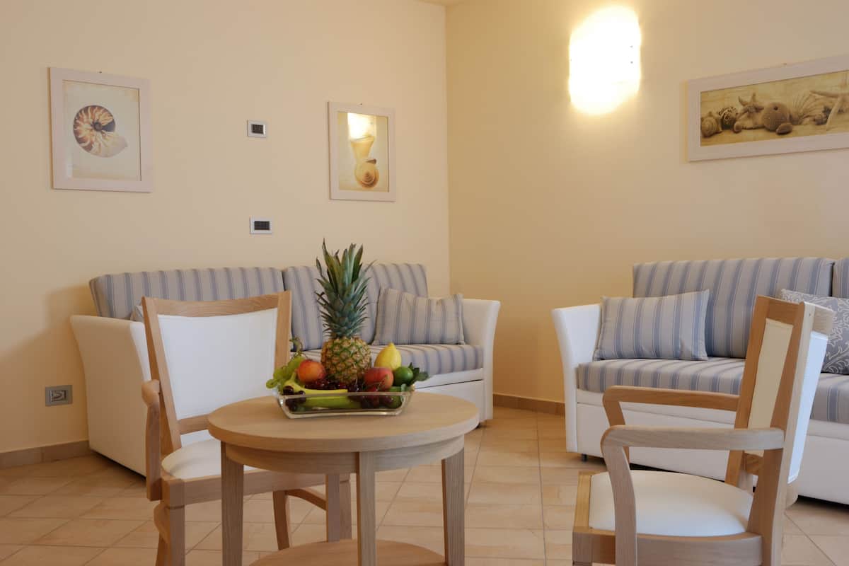 Un salon avec deux canapés, une table en bois sur laquelle sont disposés des fruits, et des œuvres d’art accrochées au mur.