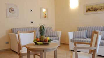 Una sala de estar con dos sofás, una mesa de madera con fruta y obras de arte colgadas en la pared.