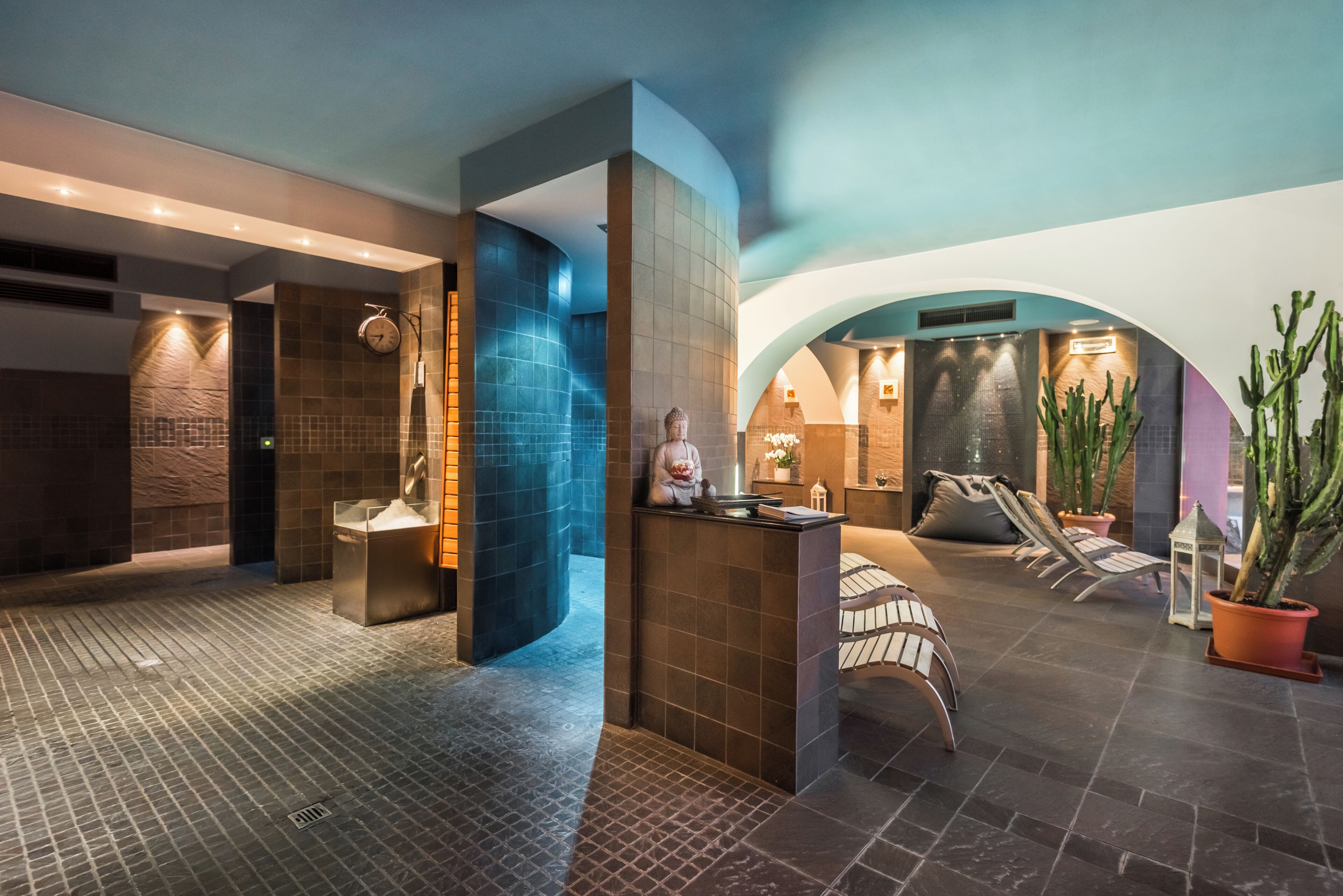 A modern spa area with a reception desk, seating area, and a large plant.
