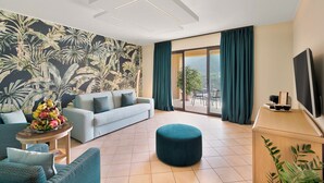 Een moderne woonkamer met een bank, poef en een tafel met fruit. Er is een balkon met uitzicht op het landschap.