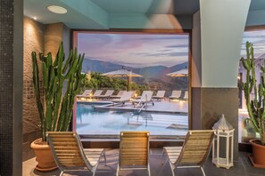Zona junto a la piscina con sillones de descanso y vistas a un paisaje montañoso.