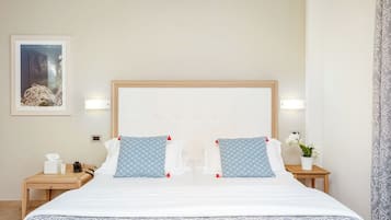 Une chambre d’hôtel avec un grand lit, deux tables de chevet, une petite table à côté du lit avec une lampe, un tableau encadré au mur et une plante en pot.