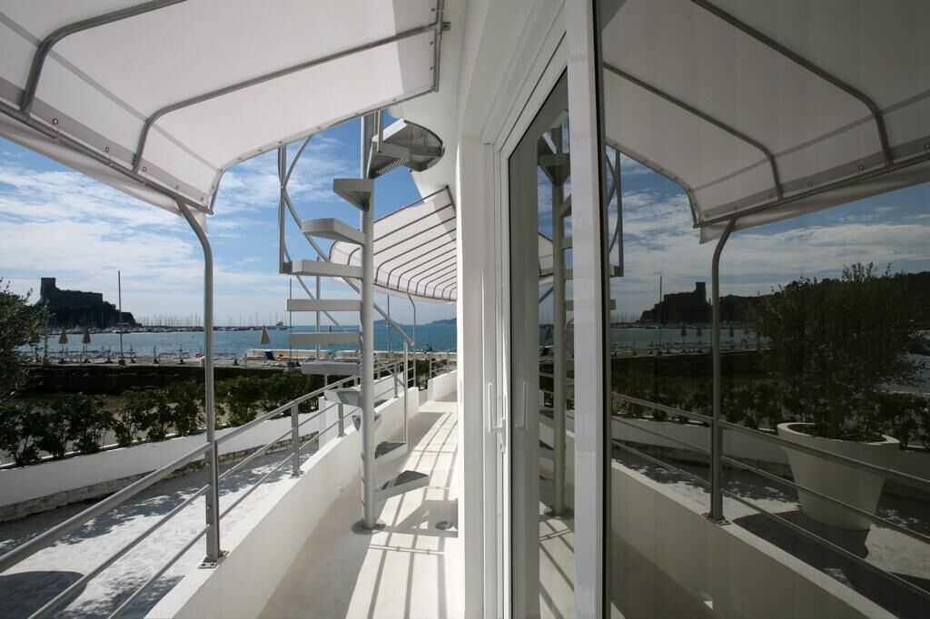 Un balcón moderno al aire libre con baranda de metal, ventanas amplias y vistas al mar y al paisaje urbano.