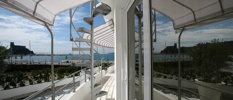 Un balcón moderno al aire libre con baranda de metal, ventanas amplias y vistas al mar y al paisaje urbano.