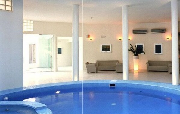 A modern indoor swimming pool with a clear view of the adjacent living area, featuring a sofa and a potted plant. - Piccolo Hotel Del Lido (Lerici)