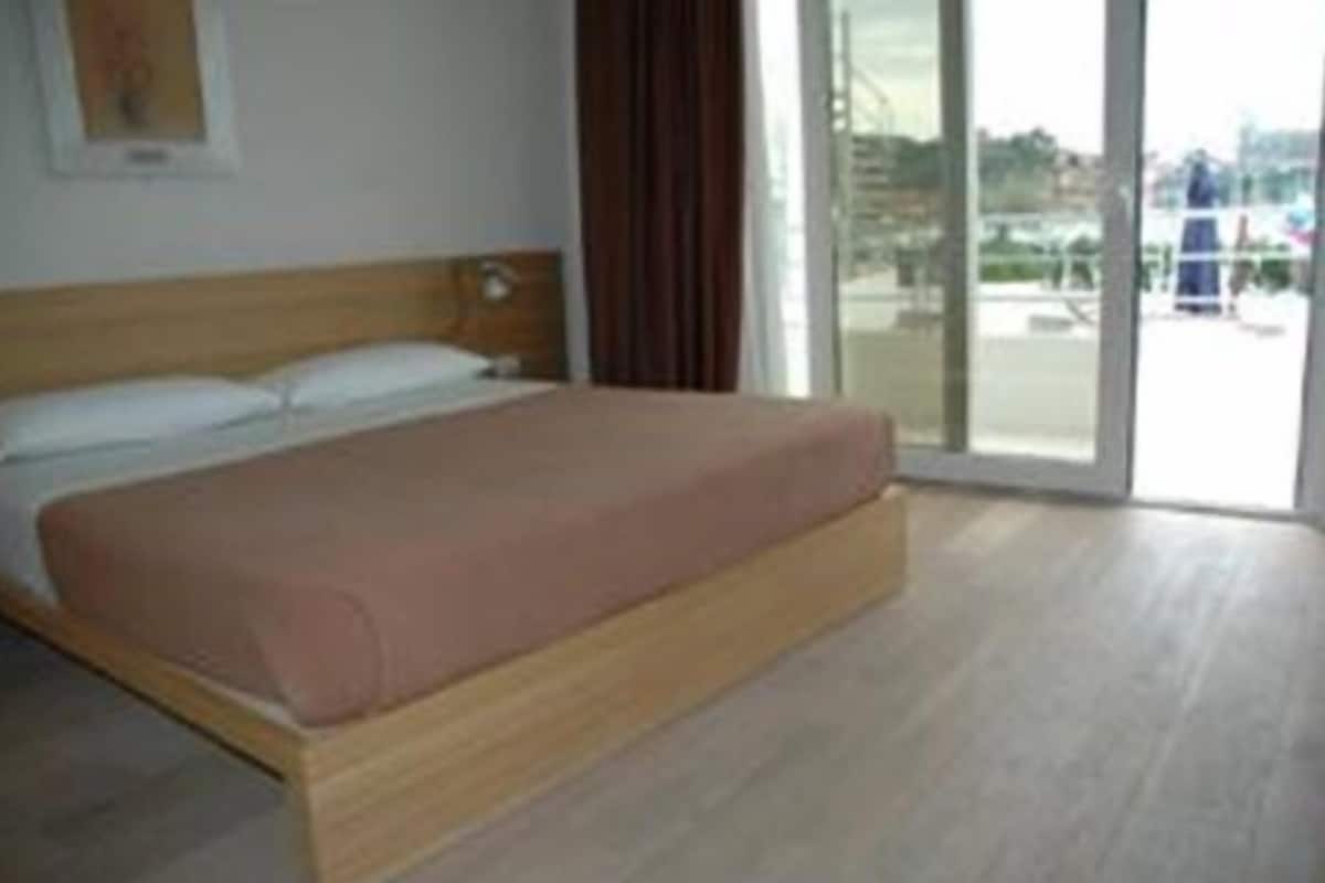 A single bed in a room with a wooden headboard, a large window, and a view of the outdoors.