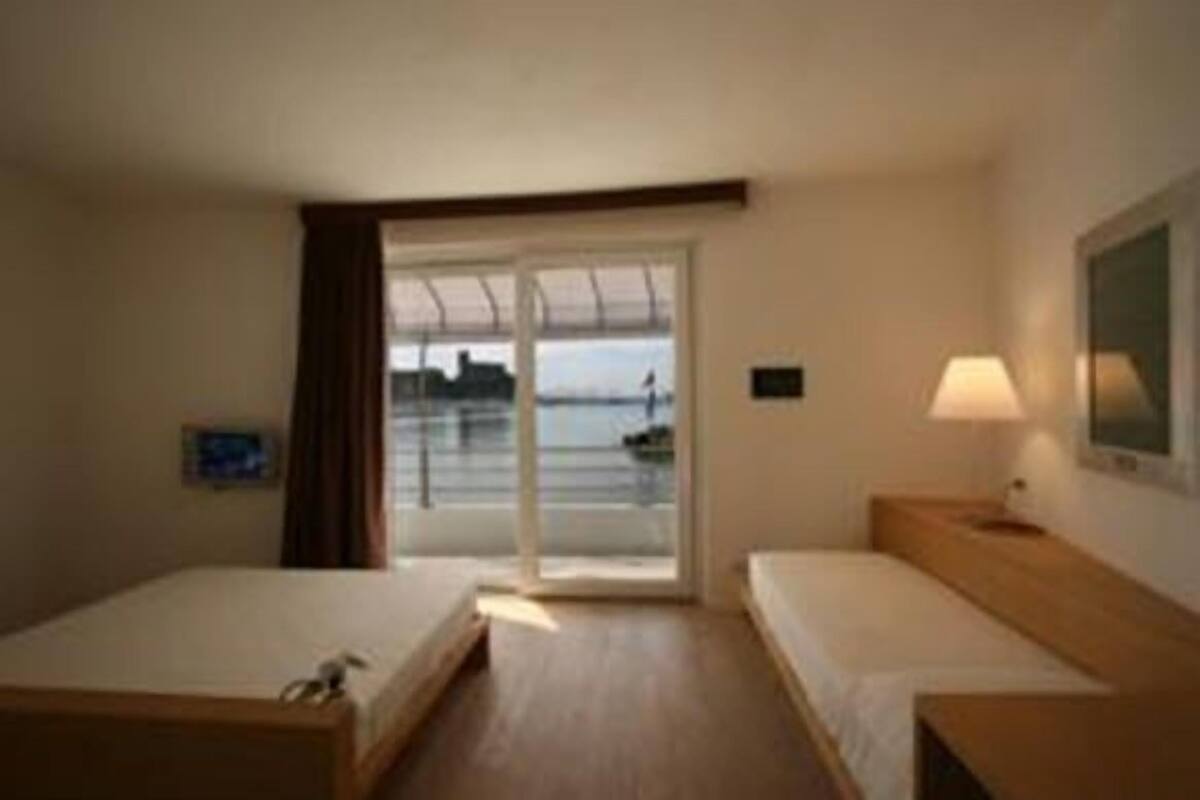 A hotel room with two beds, a window with a view of the sea, and a lamp on the nightstand.