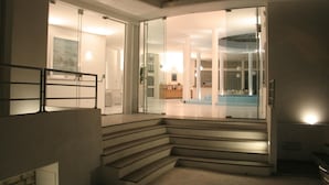 Un intérieur moderne avec un escalier menant à l’espace de vie, une entrée avec une porte en verre et une piscine visible.
