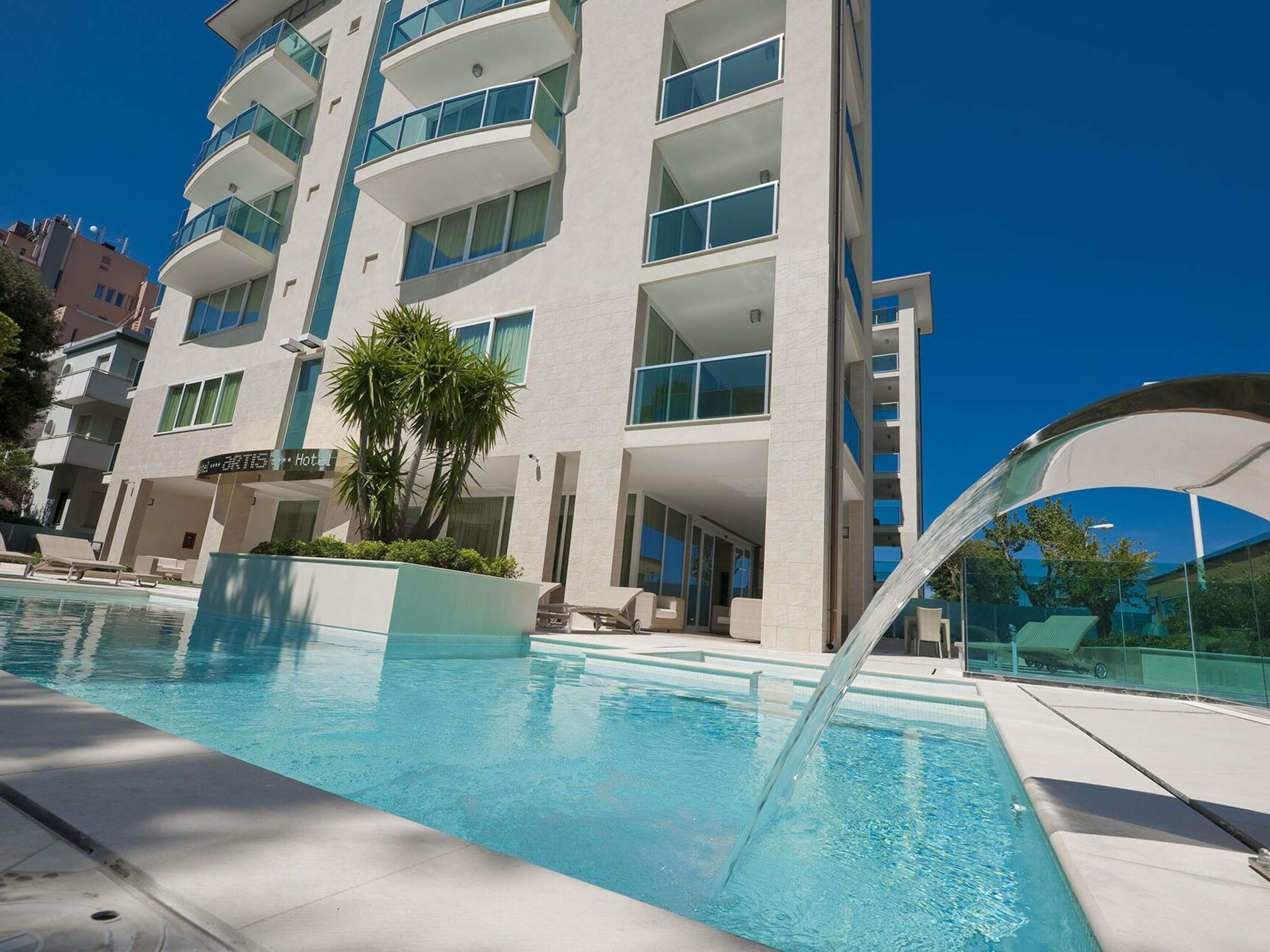 A hotel with a pool, multiple balconies, and a clear blue sky.