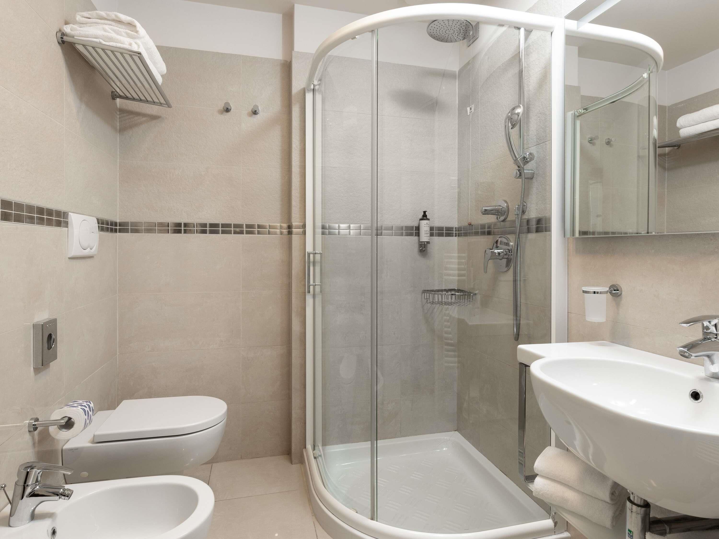 A modern bathroom with a glass-enclosed shower, a toilet, a bidet, and a sink.