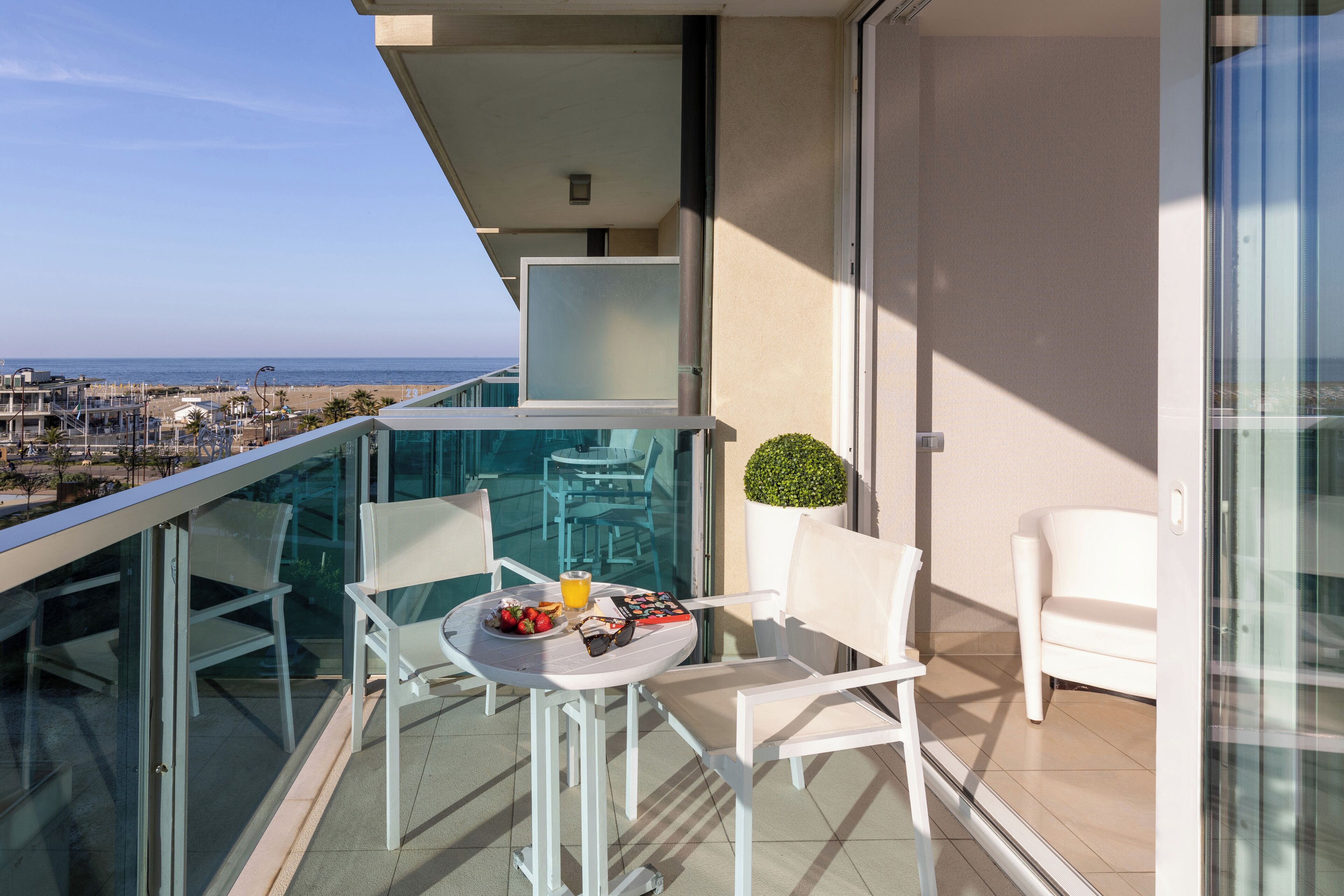 Un balcón con una mesa para dos, una pequeña planta en maceta y vistas despejadas a la playa y al paisaje urbano.