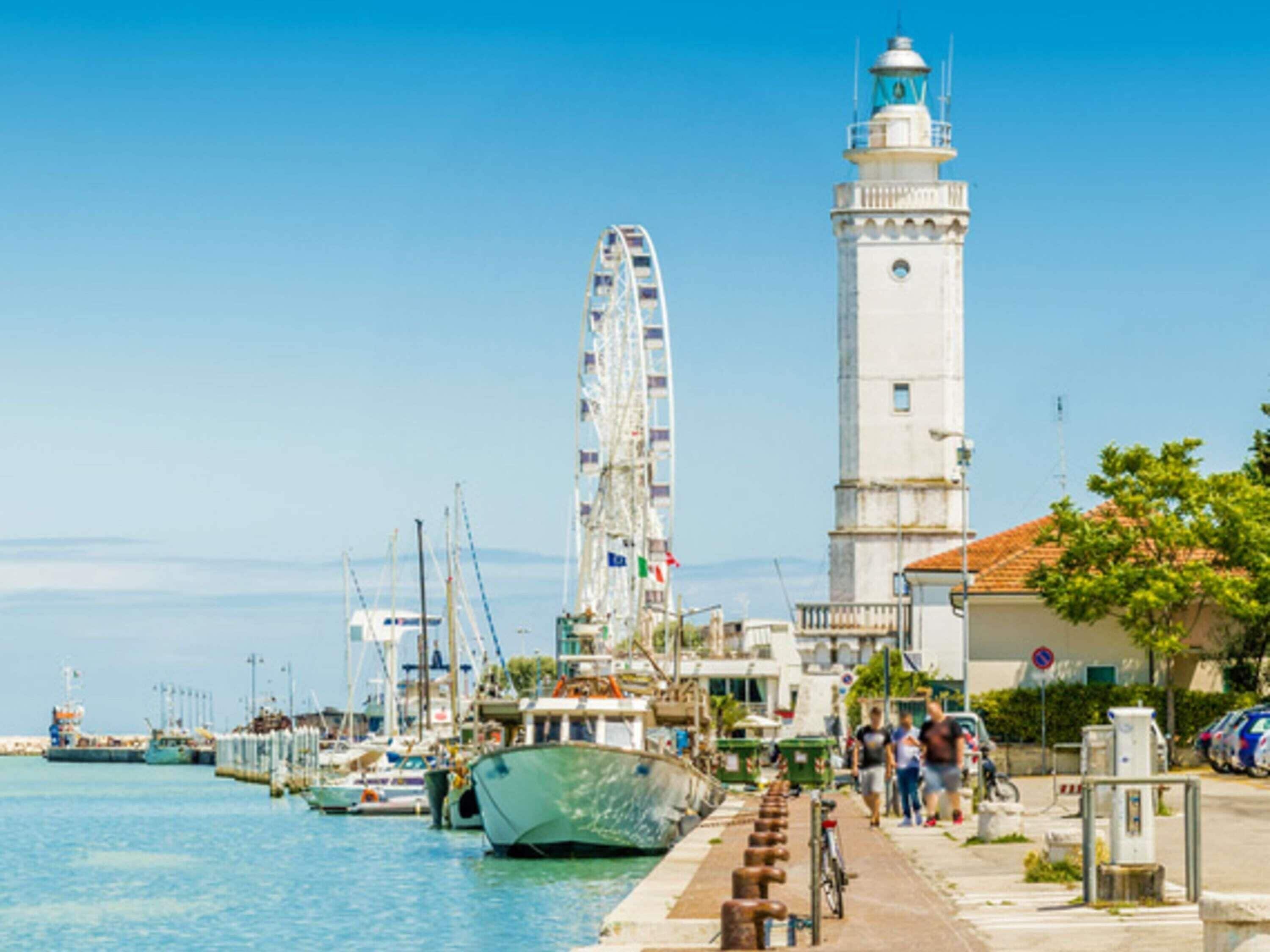 A waterfront marina with boats, a lighthouse, and a Ferris wheel.